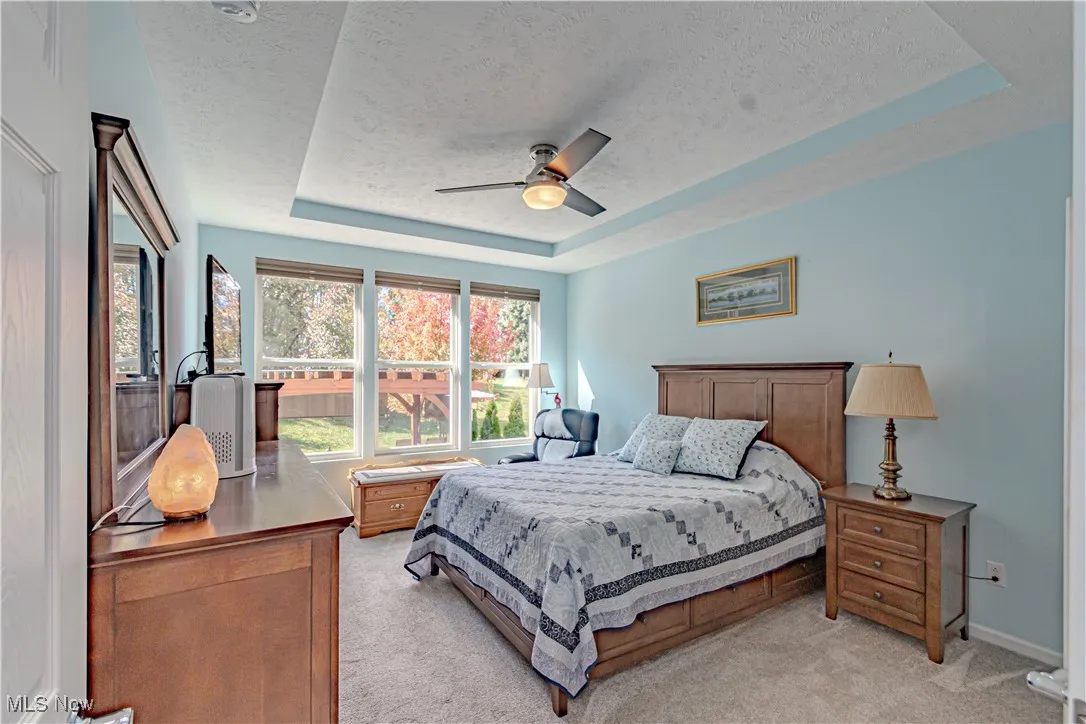 Bedroom with a tray ceiling, light carpet, ceiling fan, and a textured ceiling