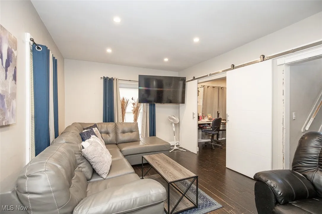 Living area with a barn door, dark wood-type flooring, recessed lighting, and a desk