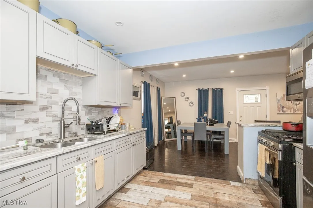 Kitchen with appliances with stainless steel finishes, backsplash, light wood-type flooring, light stone countertops, and recessed lighting