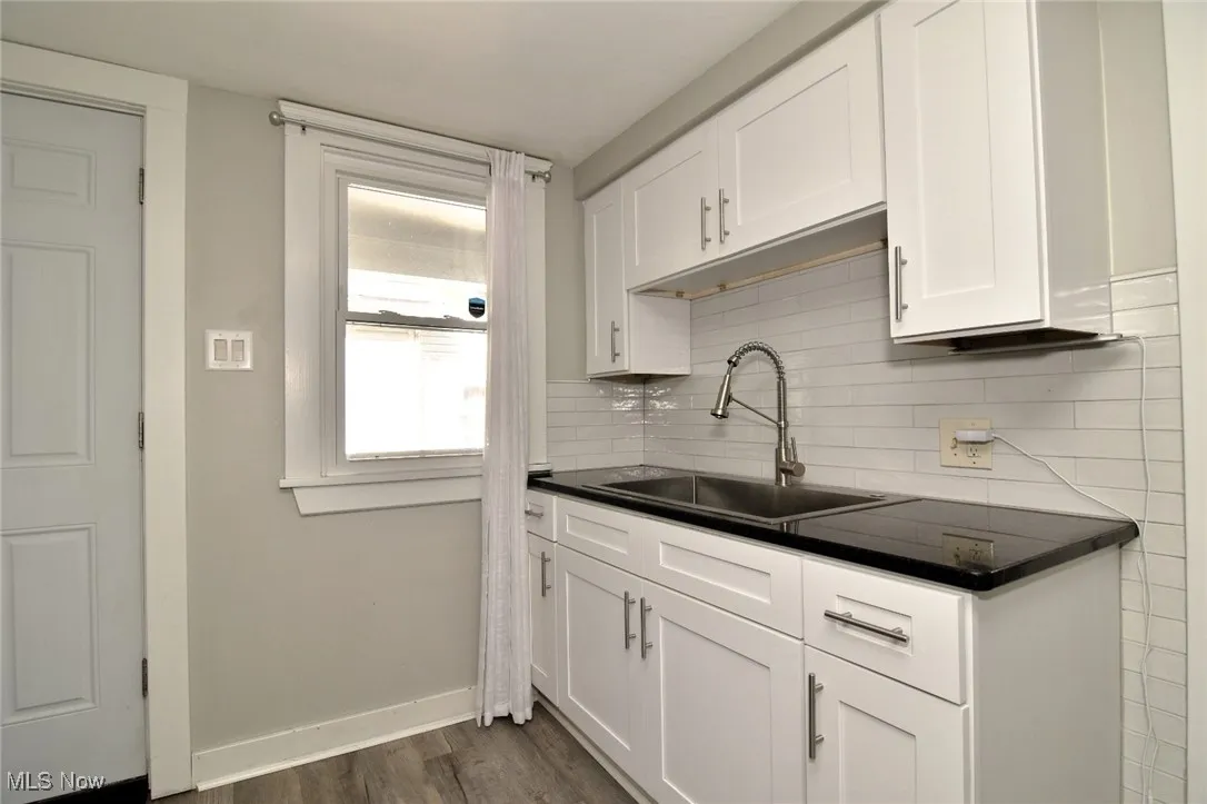 Kitchen with dark countertops, white cabinets, backsplash, and dark wood finished floors