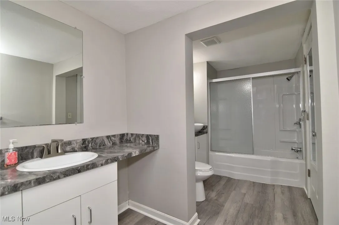 Full bath with vanity, bath / shower combo with glass door, and light wood-style floors