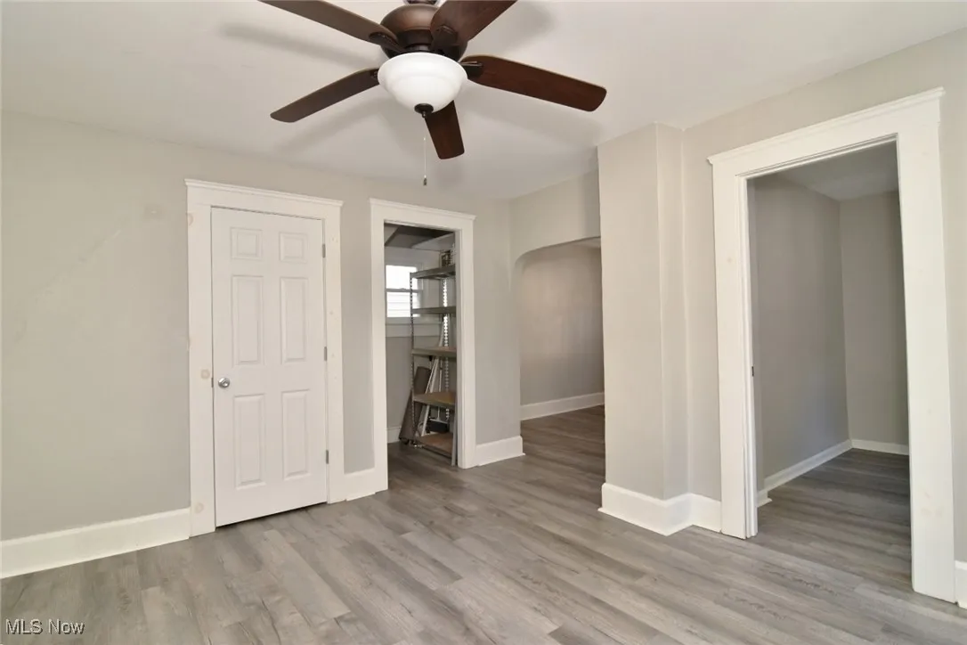 Unfurnished bedroom with light wood finished floors, arched walkways, a ceiling fan, and connected bathroom
