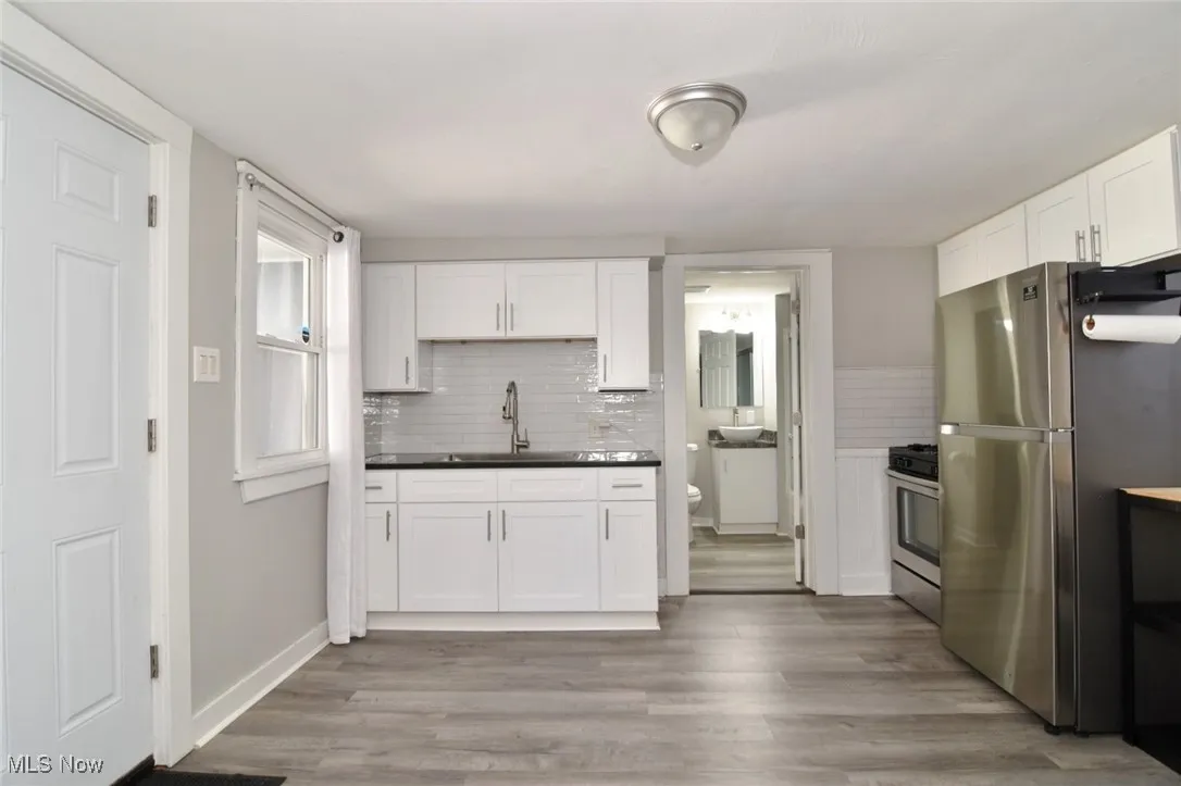 Kitchen featuring appliances with stainless steel finishes, backsplash, white cabinetry, and dark countertops