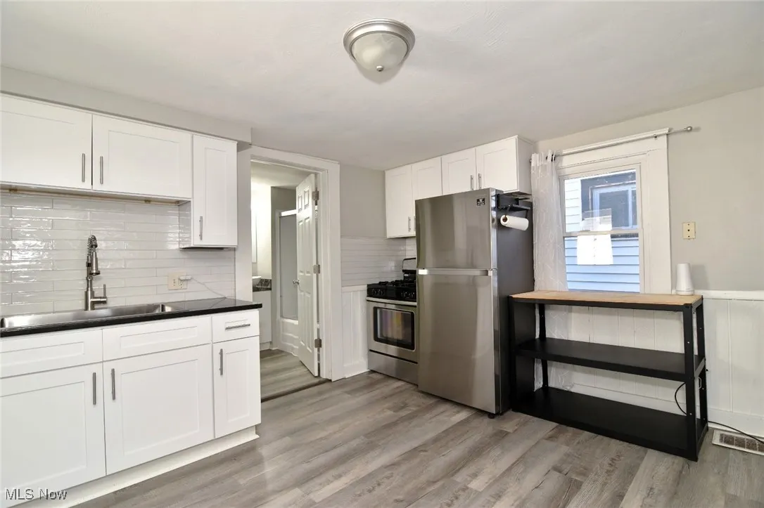 Kitchen featuring stainless steel appliances, white cabinets, tasteful backsplash, and light wood-style flooring