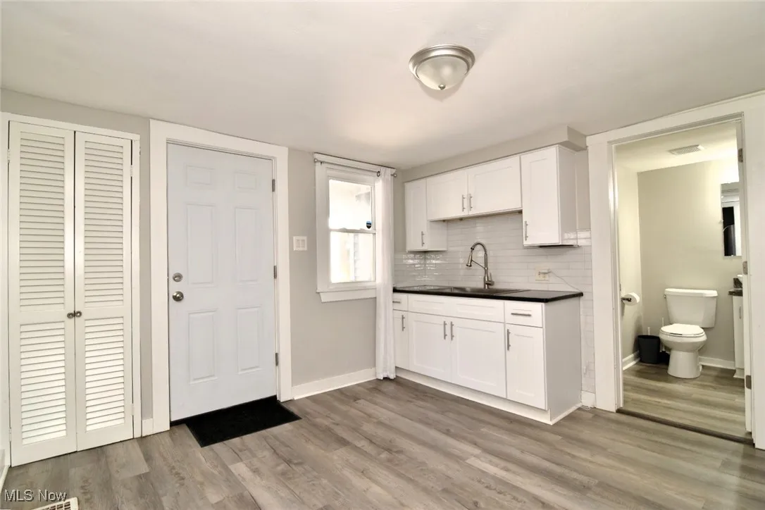 Kitchen with dark countertops, decorative backsplash, white cabinetry, and light wood-style floors