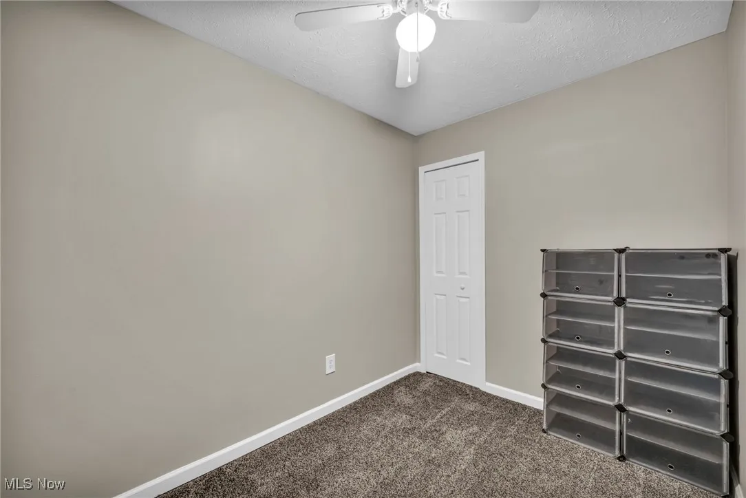Unfurnished bedroom featuring dark carpet, a textured ceiling, and a ceiling fan