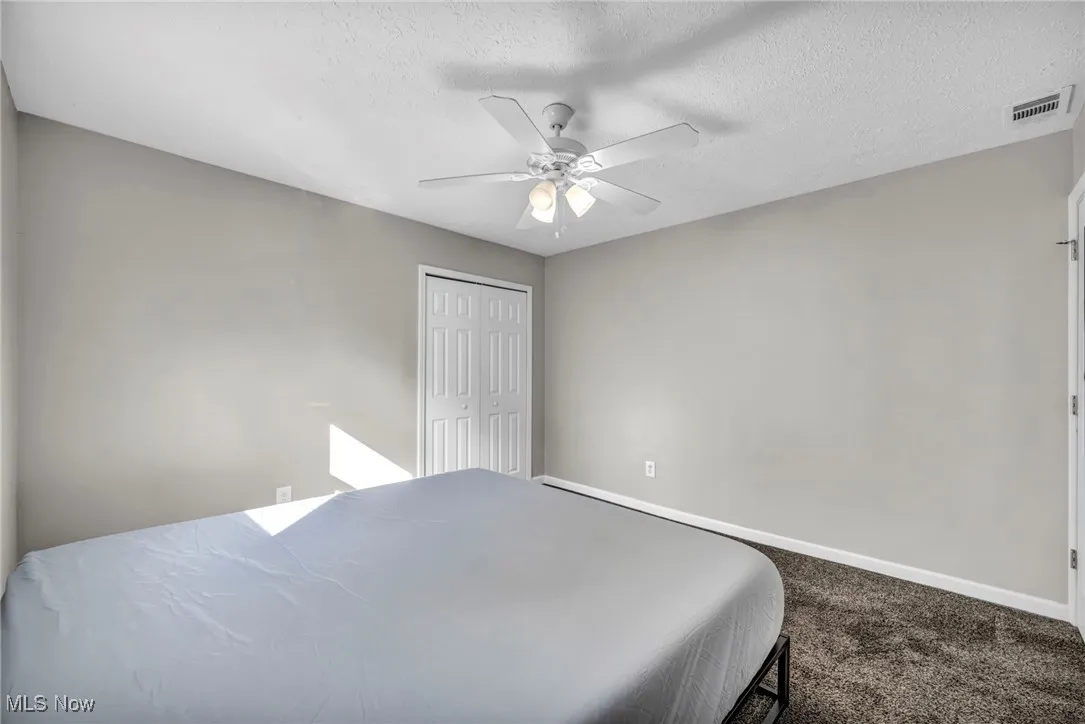 Bedroom featuring dark colored carpet, a textured ceiling, a closet, and a ceiling fan