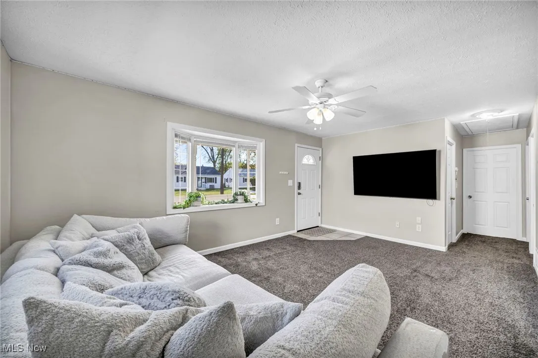 Carpeted living area featuring attic access, a ceiling fan, and a textured ceiling