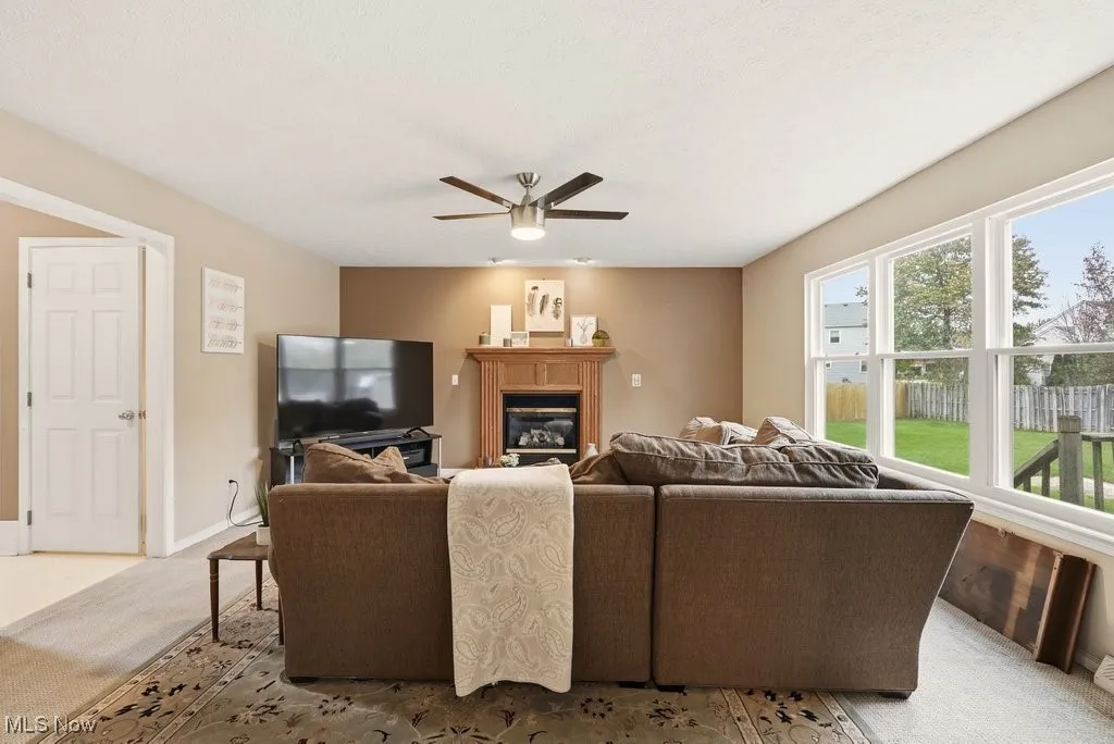Living room with carpet flooring, a glass covered fireplace, and a ceiling fan