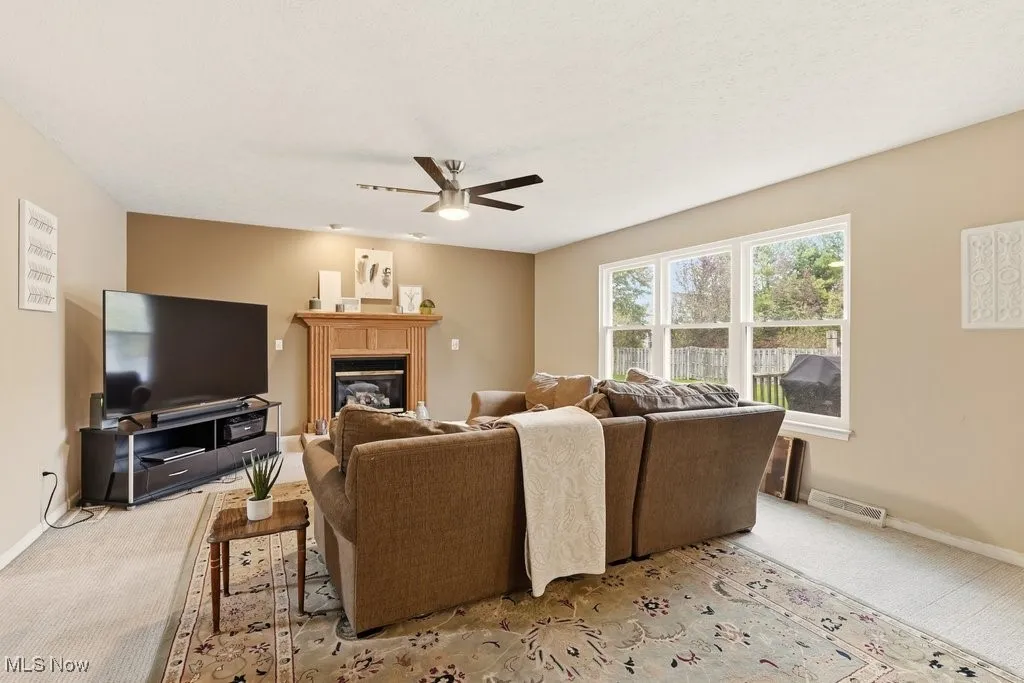 Living area featuring carpet flooring, a glass covered fireplace, and ceiling fan