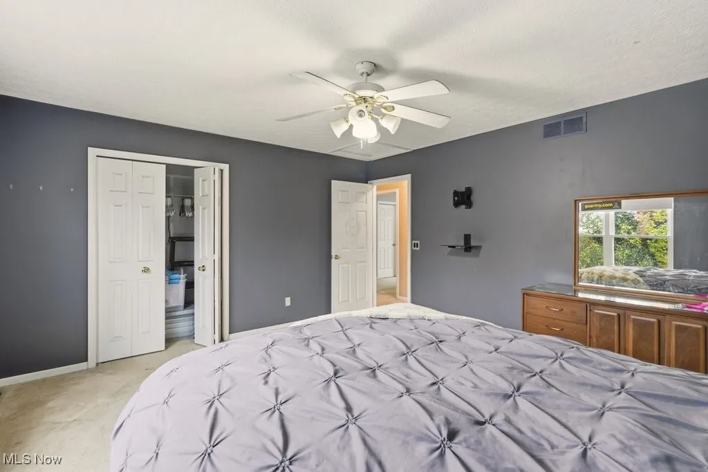 Bedroom with light colored carpet, ceiling fan, and a textured ceiling
