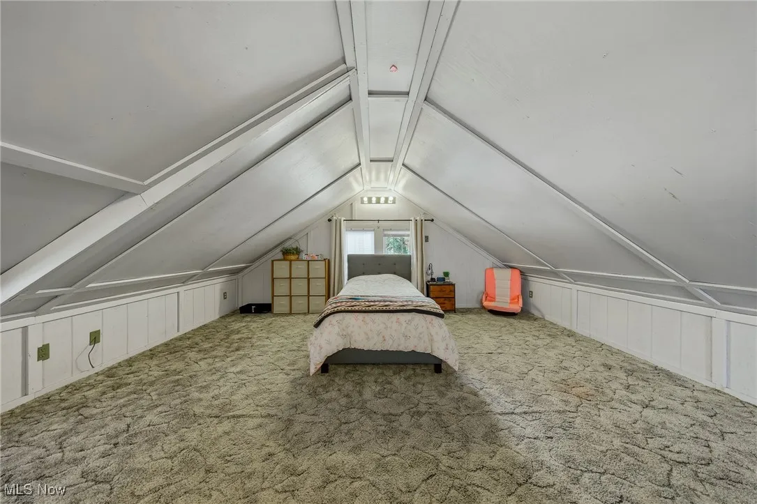 Bedroom with carpet flooring, vaulted ceiling, and a decorative wall