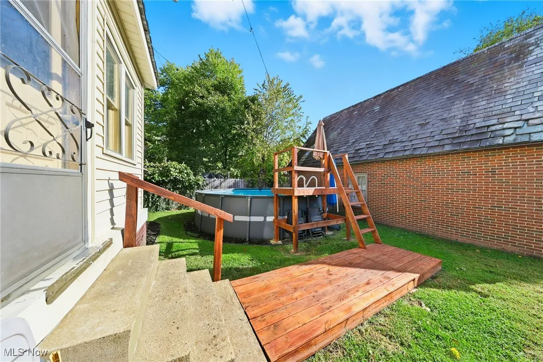 View of playground featuring a wooden deck, an outdoor pool, and a lawn