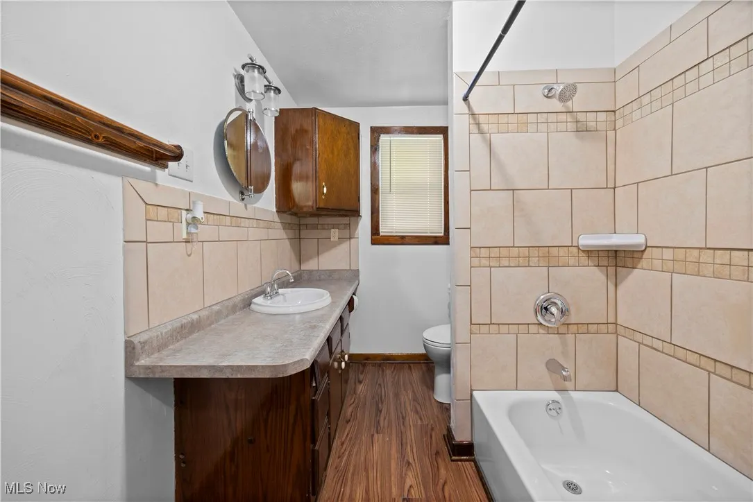 Bathroom with decorative backsplash, bathing tub / shower combination, dark wood finished floors, and vanity