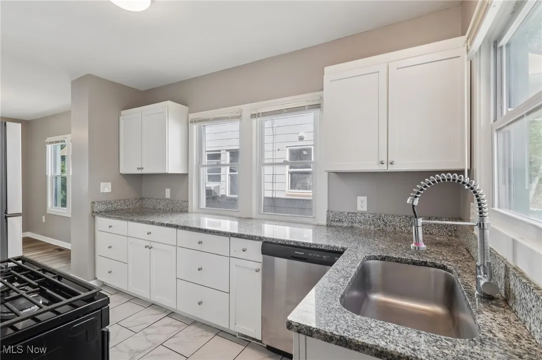 Kitchen featuring black range with gas cooktop, white cabinetry, stainless steel dishwasher, and plenty of natural light