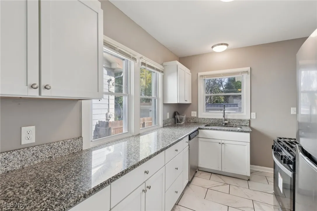 Kitchen with light stone counters, white cabinets, appliances with stainless steel finishes, and light marble finish flooring