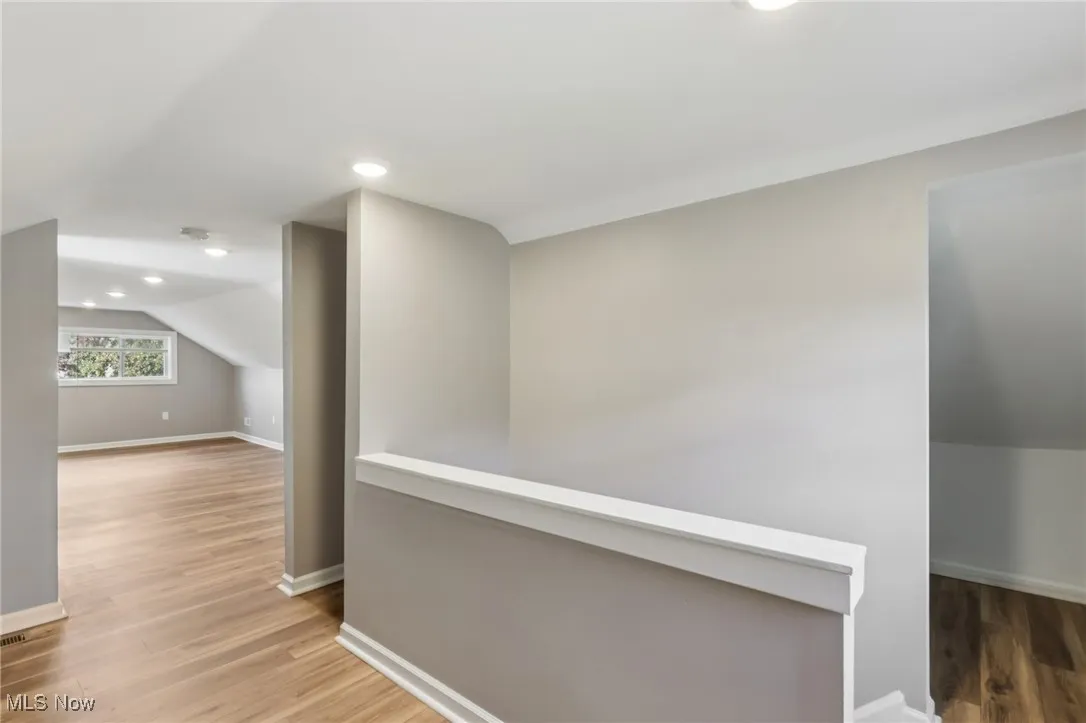 Hall featuring light wood-style flooring, vaulted ceiling, recessed lighting, and an upstairs landing