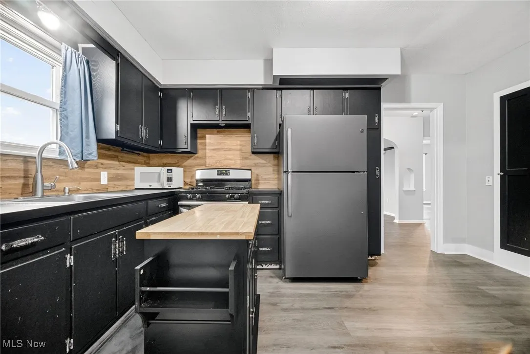 Kitchen with dark cabinetry, appliances with stainless steel finishes, light wood finished floors, and decorative backsplash