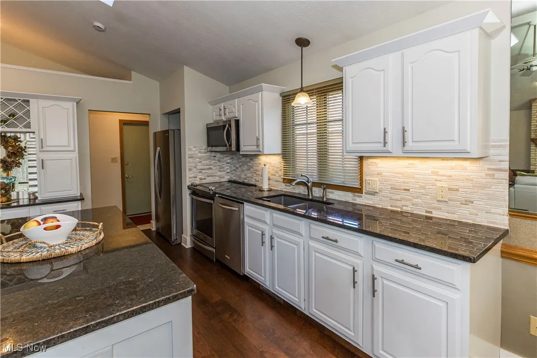 Kitchen featuring dark stone counters, dark wood-type flooring, decorative light fixtures, white cabinets, and decorative backsplash