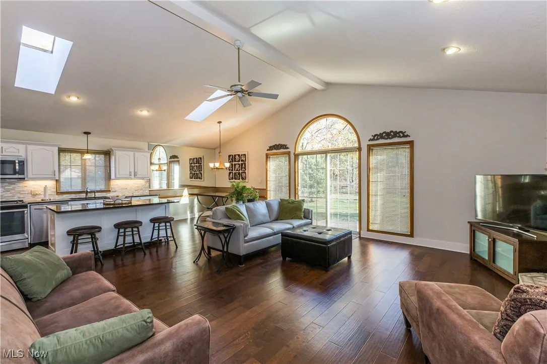 Living area with beam ceiling, recessed lighting, dark wood finished floors, high vaulted ceiling, and a skylight