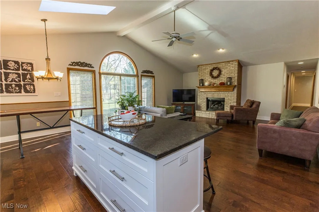 Kitchen featuring white cabinetry, a breakfast bar, dark stone countertops, a brick fireplace, and pendant lighting