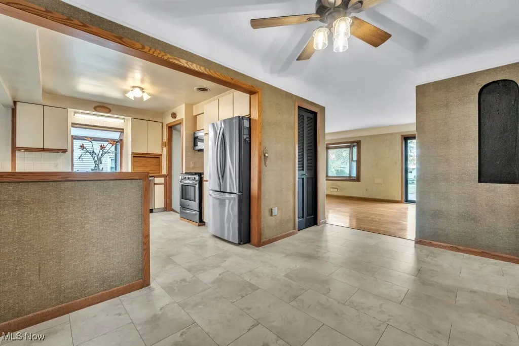Kitchen with appliances with stainless steel finishes, a ceiling fan, white cabinetry, and wallpapered walls