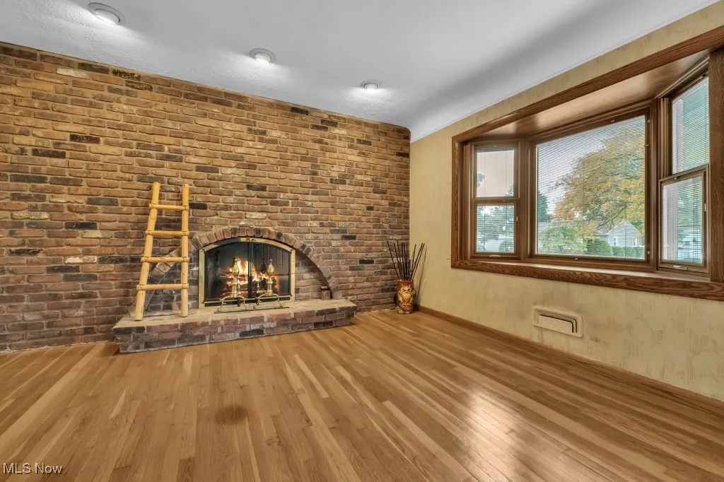 Fireplace shown is digitally staged for visualization purposes. Unfurnished living room with hardwood / wood-style flooring, a brick fireplace, and brick wall