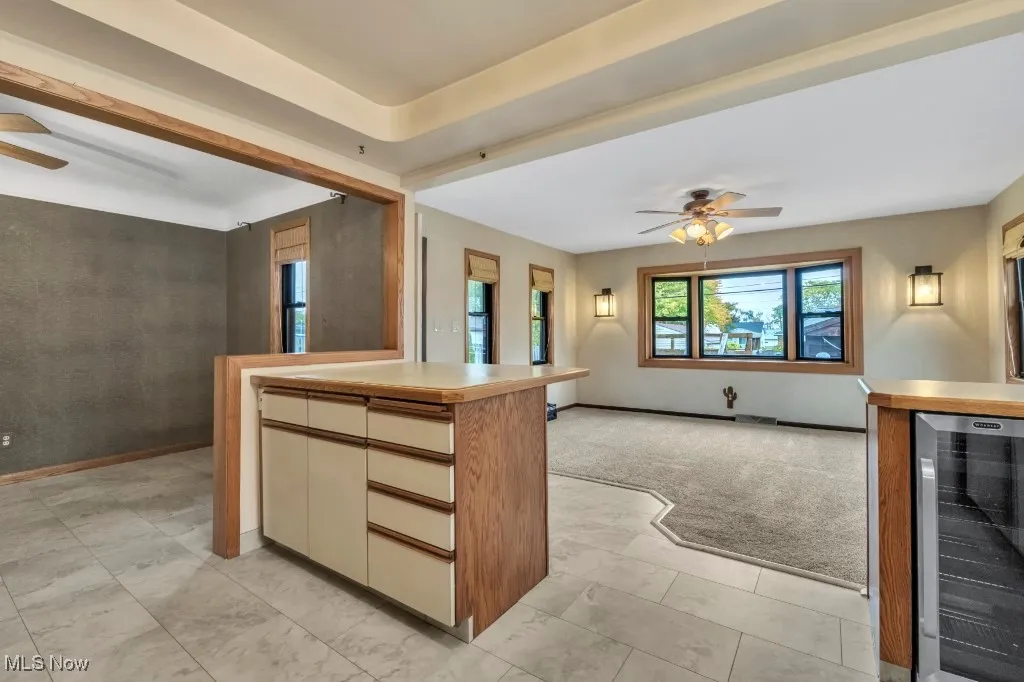 Kitchen featuring ceiling fan, beverage cooler, open floor plan, vinyl flooring, light carpet, and light countertops