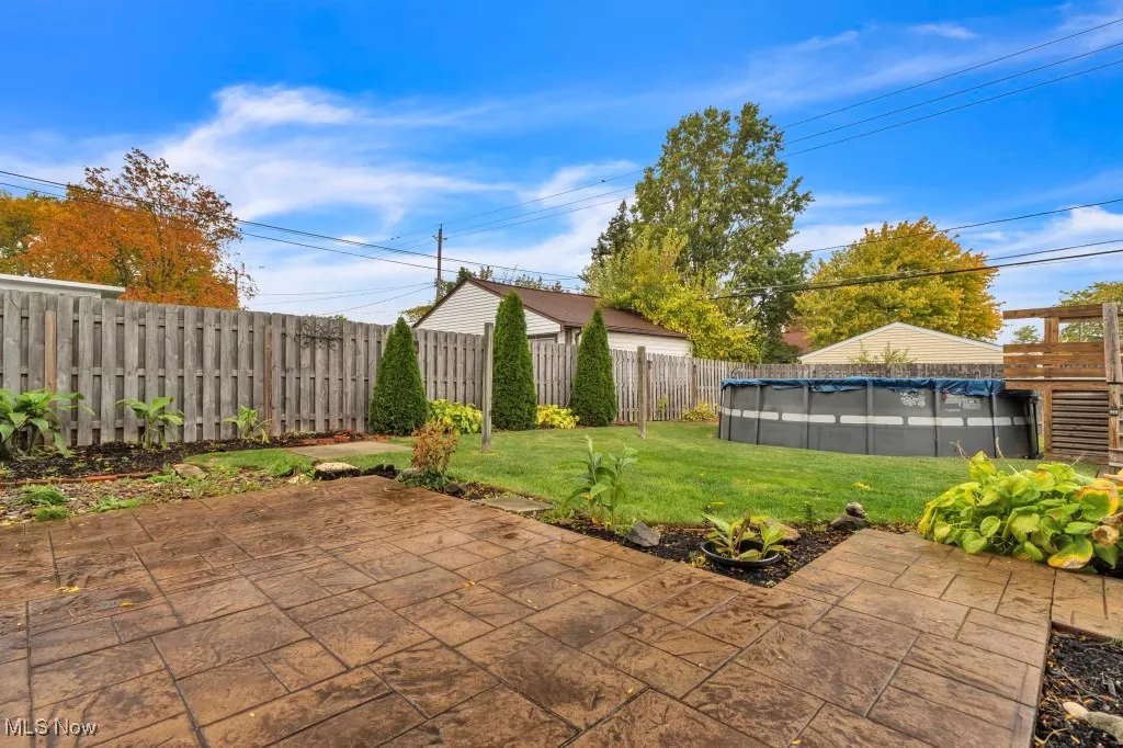 Wooden fenced backyard featuring a stamped concrete patio and above ground pool.