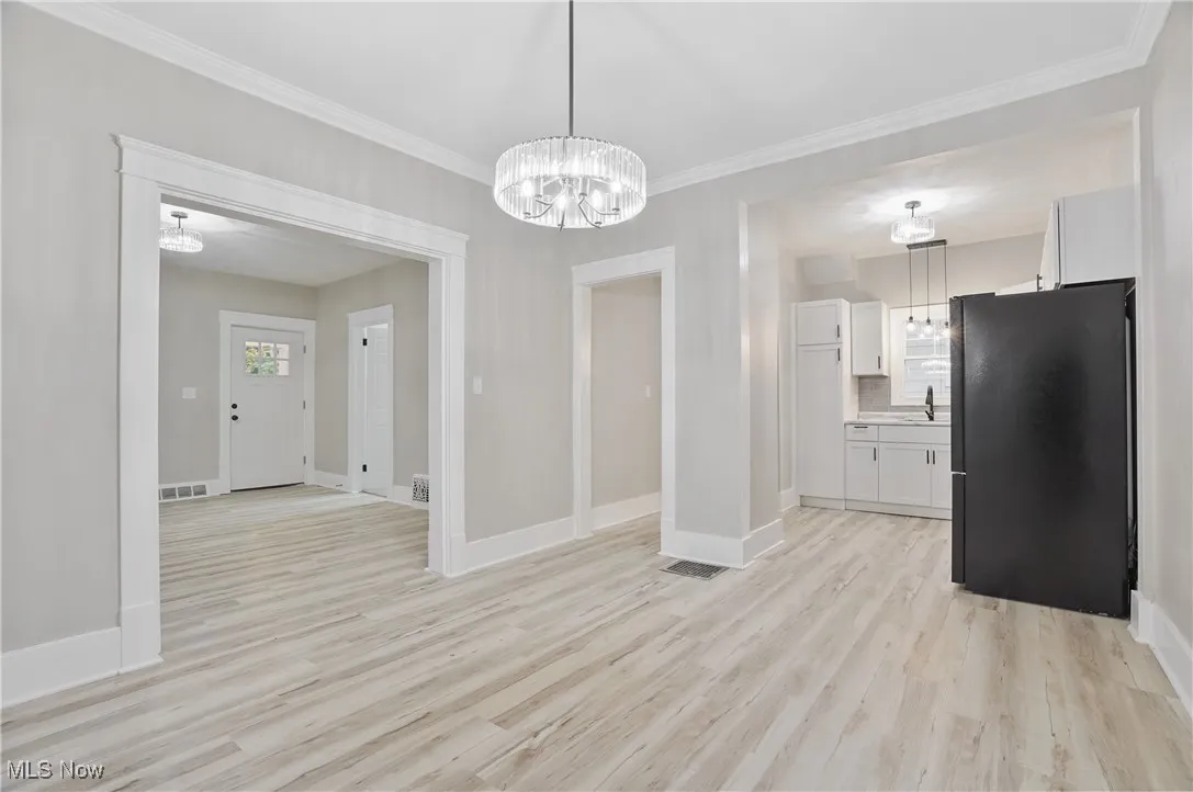 Unfurnished dining area with light wood-style flooring, crown molding, and a chandelier