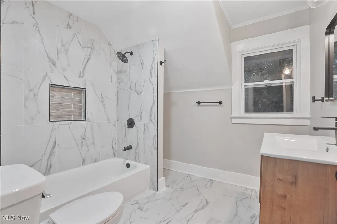 Bathroom with vanity, washtub / shower combination, light marble finish flooring, and ornamental molding
