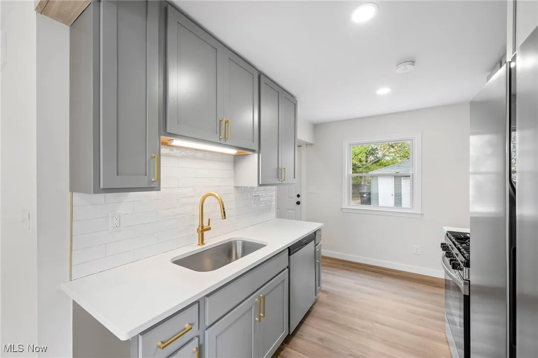 Kitchen featuring gray cabinets, tasteful backsplash, appliances with stainless steel finishes, LVP floors, and light stone counters
