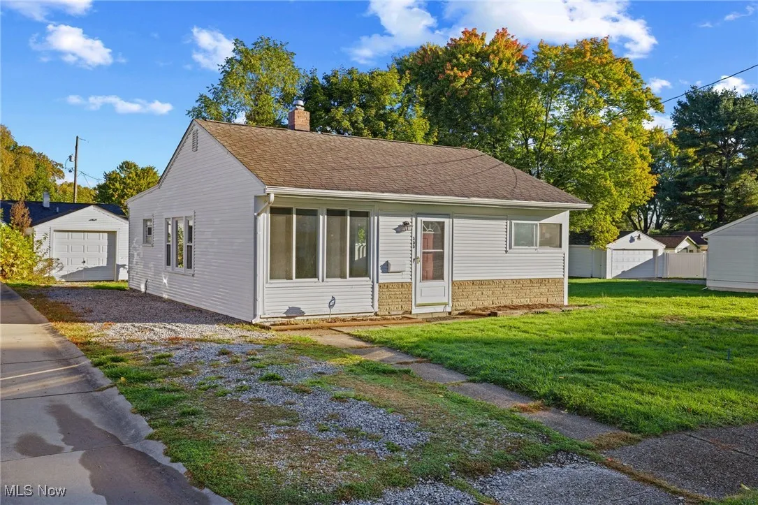 Bungalow-style house with a front lawn, a chimney, an outdoor structure, stone siding, and a detached garage