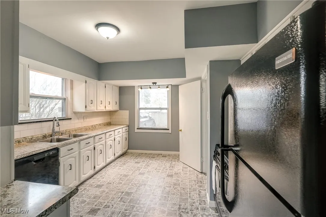 Kitchen featuring black appliances, tasteful backsplash, white cabinetry, and light countertops.