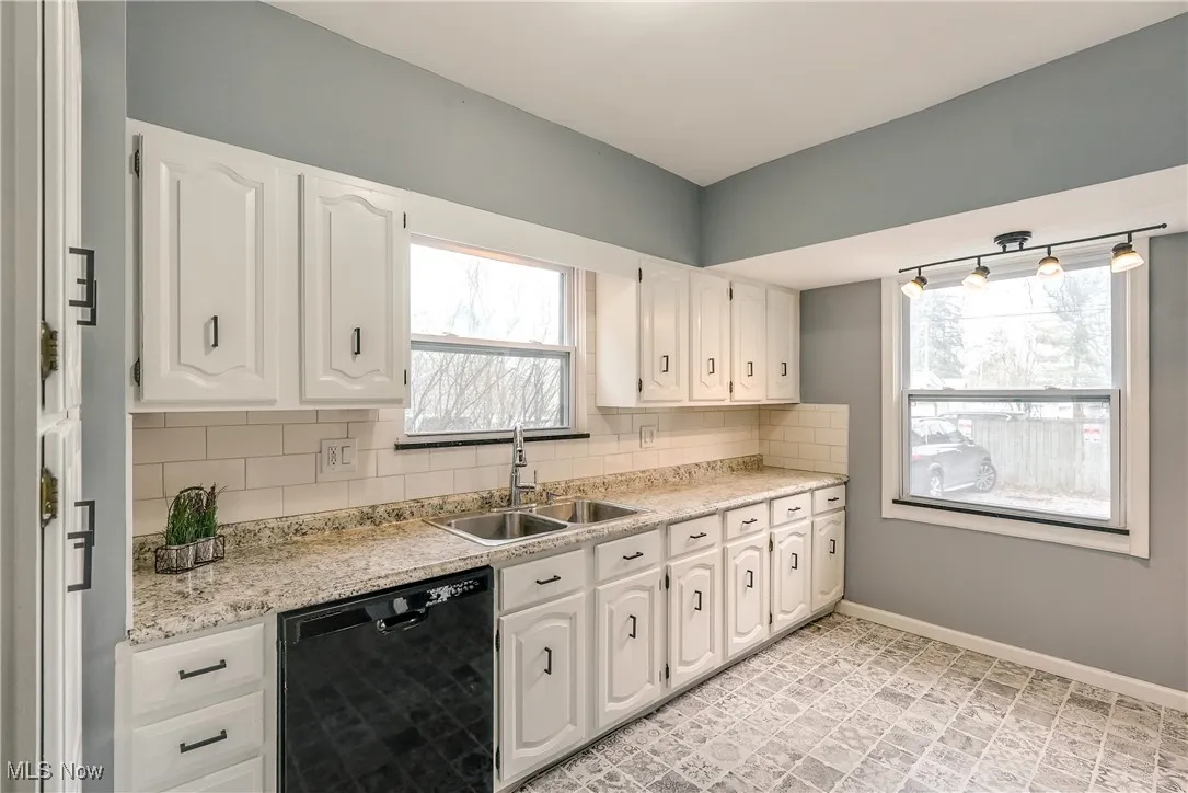 Kitchen featuring tasteful backsplash, black dishwasher, healthy amount of natural light, and white cabinetry.