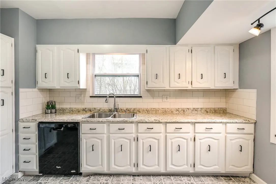 Kitchen with decorative backsplash, black dishwasher, light countertops, and white cabinets