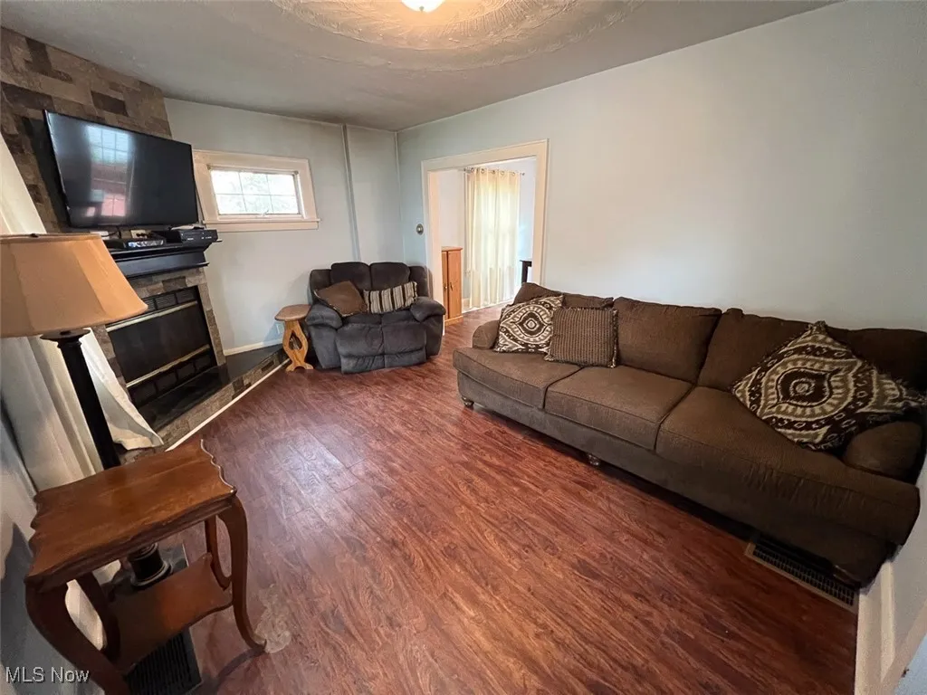 Living room featuring dark wood-style floors and a stone fireplace