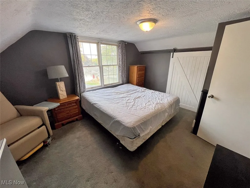 Bedroom featuring a barn door, carpet floors, vaulted ceiling, and a textured ceiling
