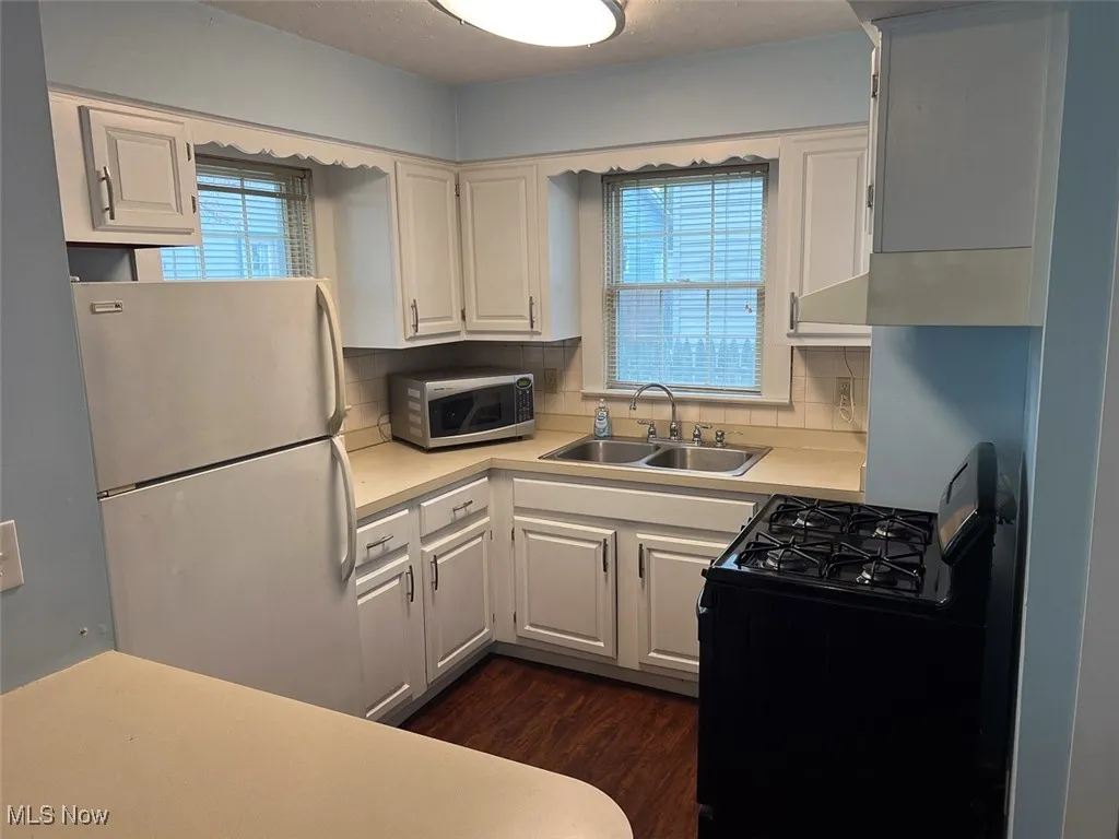 Kitchen featuring light countertops, gas stove, freestanding refrigerator, stainless steel microwave, and dark wood-style floors