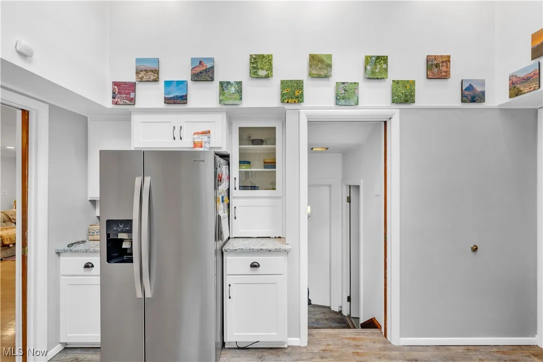 Kitchen with stainless steel refrigerator with ice dispenser, white cabinetry, light wood-style floors, and light stone countertops