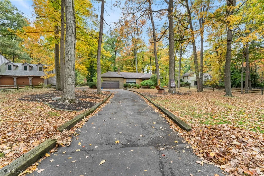 View of front of property with a garage, view of wooded area, and asphalt driveway