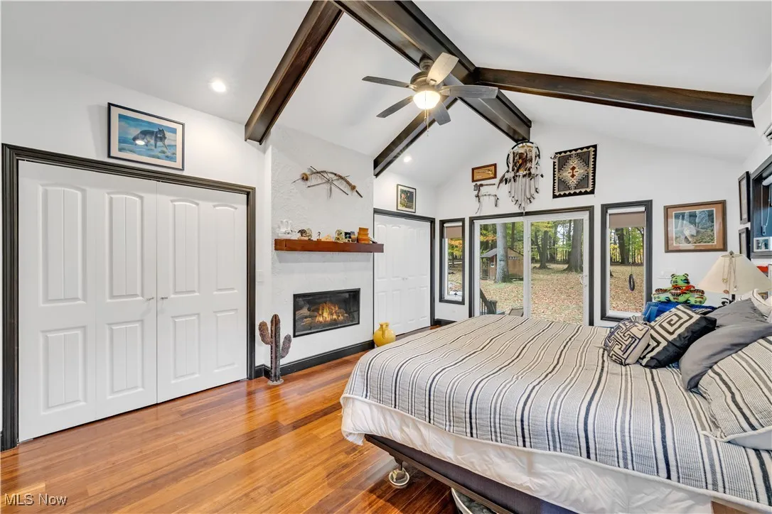 Bedroom featuring beamed ceiling, wood finished floors, a large fireplace, ceiling fan, and a closet