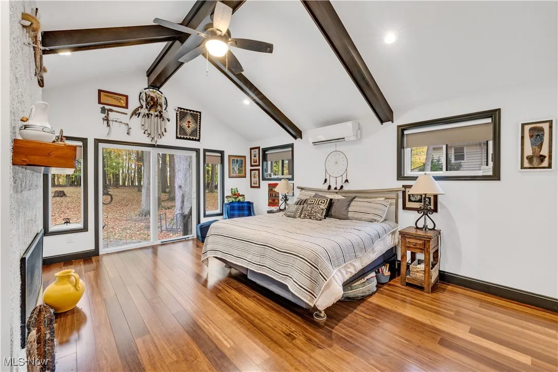 Bedroom featuring beamed ceiling, multiple windows, hardwood / wood-style floors, high vaulted ceiling, and a wall mounted air conditioner