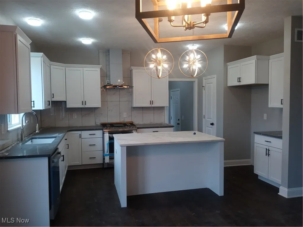 Kitchen featuring exhaust hood, decorative light fixtures, range, a kitchen island, and white cabinets