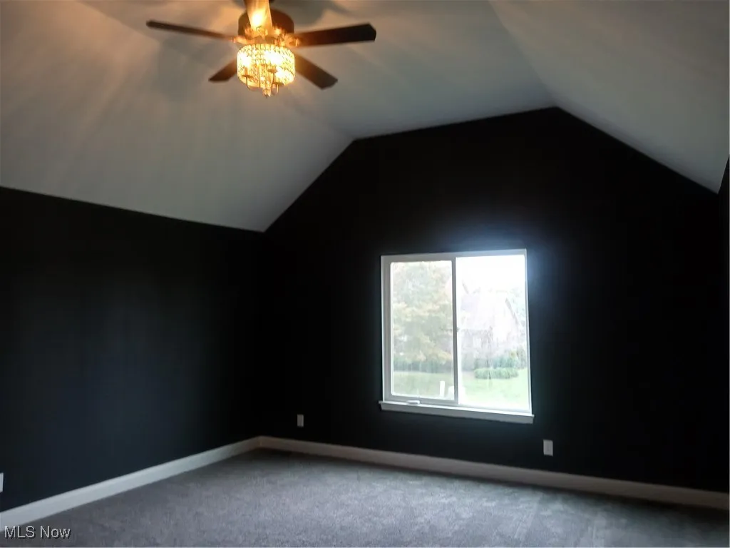 Carpeted spare room featuring vaulted ceiling and ceiling fan