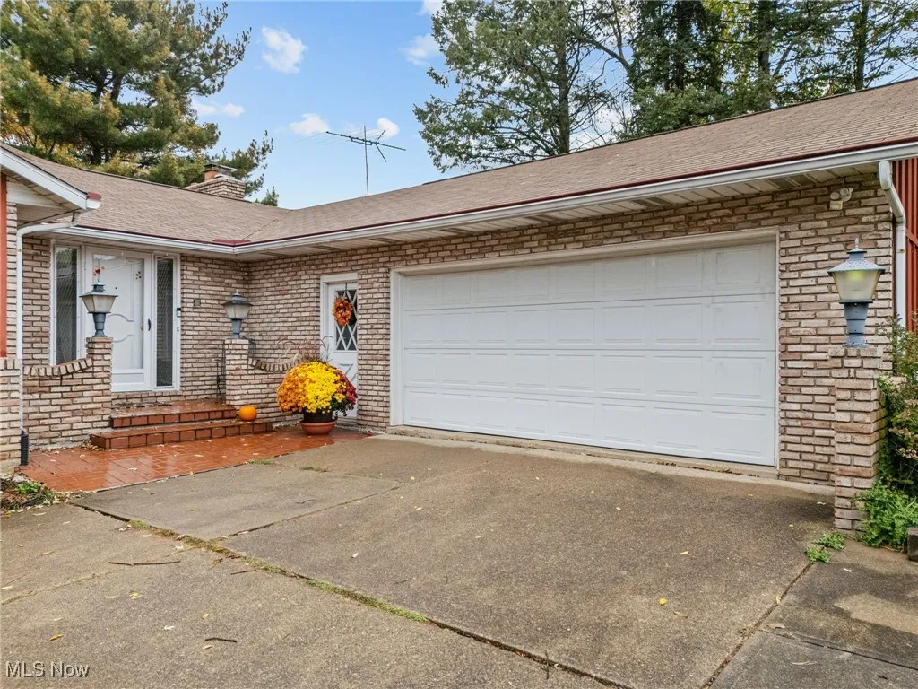 Single story home featuring driveway, a shingled roof, a chimney, brick siding, and an attached garage