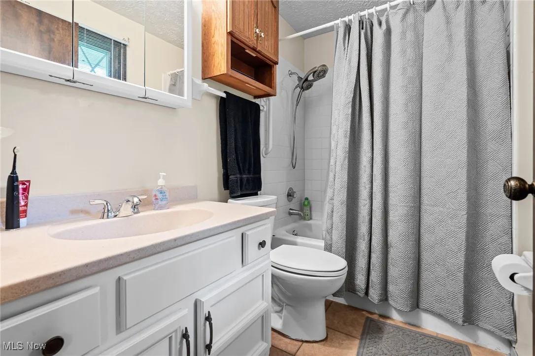 Master Full bathroom with vanity, shower / tub combo with curtain, light tile patterned flooring, and a textured ceiling