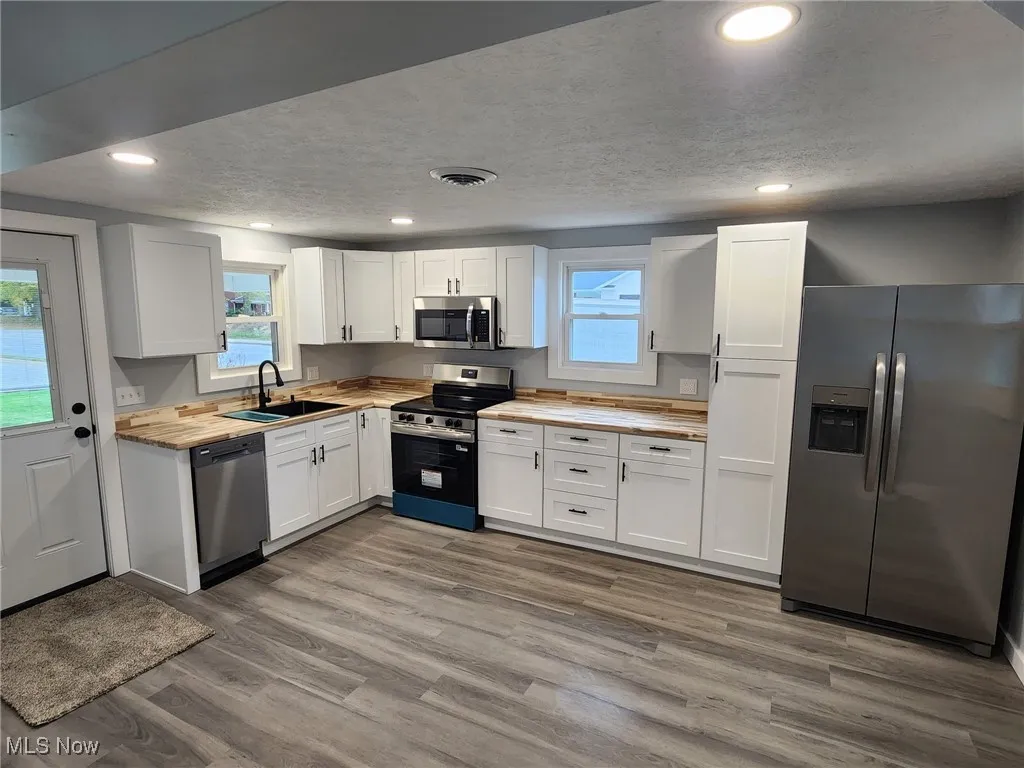 Kitchen featuring stainless steel appliances, white cabinets, butcher block countertops, dark wood-style floors, and a textured ceiling