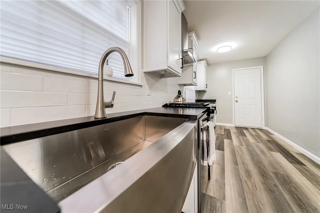 Kitchen featuring white cabinetry, dark wood-style flooring, tasteful backsplash, wall chimney exhaust hood, and dark stone counters
