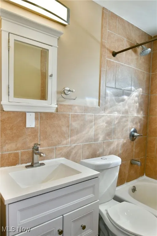 Full bathroom featuring shower / tub combination, vanity, backsplash, and tile walls